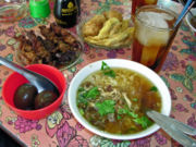 A selection of Indonesian food, including Soto Ayam (chicken noodle soup), sate kerang (shellfish kebabs), telor pindang (preserved eggs), perkedel (fritter), and es teh manis (sweet iced tea)