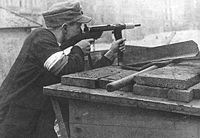 Polish insurgent, wearing armband in the national colours, at a Warsaw Uprising barricade. He is using the Polish submachine gun Błyskawica.