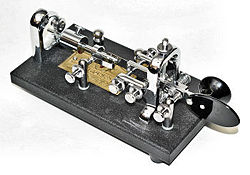 Vibroplex semiautomatic key. The paddle, when pressed to the right by the thumb, generates a series of dits, the length and timing of which are controlled by a sliding weight toward the rear of the unit. When pressed to the left by the knuckle of the index finger, the paddle generates a dah, the length of which is controlled by the operator. Multiple dahs require multiple presses. Left-handed operators use a key built as a mirror image of this one.