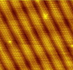 This scanning tunneling microscope image clearly shows the individual atoms that make up this gold(100) surface. Reconstruction causes the surface atoms to deviate from the bulk crystal structure and arrange in columns several atoms wide with pits between them.