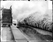 A wave breaking on the shore of Lake Michigan while a man watches from a bridge.