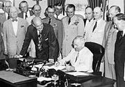President Truman signs the National Security Act Amendment of 1949 with guests in the Oval Office.