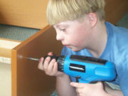 A child using a cordless handheld drill to assemble a bookcase.