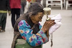 An elderly Tibetan woman holding a prayer wheel on the street in Lhasa
