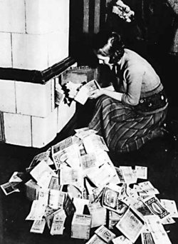Without a gold standard, governments can print as much money as they want, destroying wealth through inflation. A German woman in 1924 feeding a stove with currency notes, which burn longer than the amount of firewood they can buy.