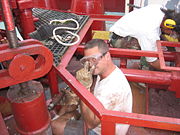 An able seaman uses a needlegun scaler while refurbishing a mooring winch at sea.