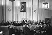 David Ben-Gurion proclaiming Israeli independence on May 14, 1948 below a portrait of Herzl