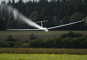 An LS4 glider crossing the finish line of a competition at high speed. It is jettisoning water that has been used as ballast.