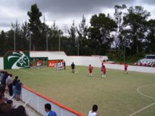 An indoor soccer game at an open air venue in Mexico. The referee has just awarded the red team a free kick.