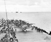 USS Kitkun Bay prepares to launch her Wildcat fighters while USS White Plains is straddled by 14 inch shells