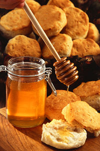 A jar of honey, shown with a wooden honey dipper and scones