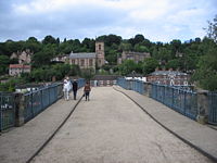 Pedestrians crossing the Iron Bridge with Ironbridge in the background.