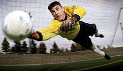 A goalkeeper dives to stop the ball from entering his goal.