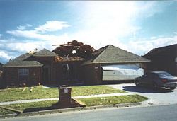 An example of EF1 damage.  Here, the roof has been substantially damaged, and the garage door blown outwards, but the walls and supporting structures are still intact.