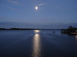 A full moon lights up the surface of a lake at night.