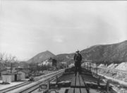 A westbound Santa Fe train pauses at Cajon Siding to cool its braking equipment after descending the pass in March 1943.  The original station structures and facilities can be seen to the left of the train.