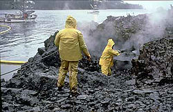 Workers using high-pressure, hot-water washing to clean an oiled shoreline.
