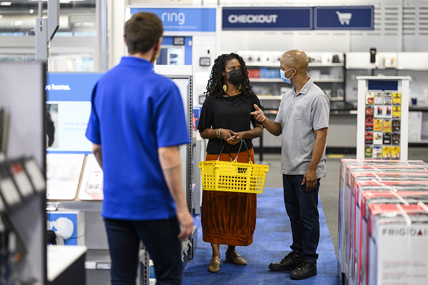 two customers shop at a best buy store as an employee looks on