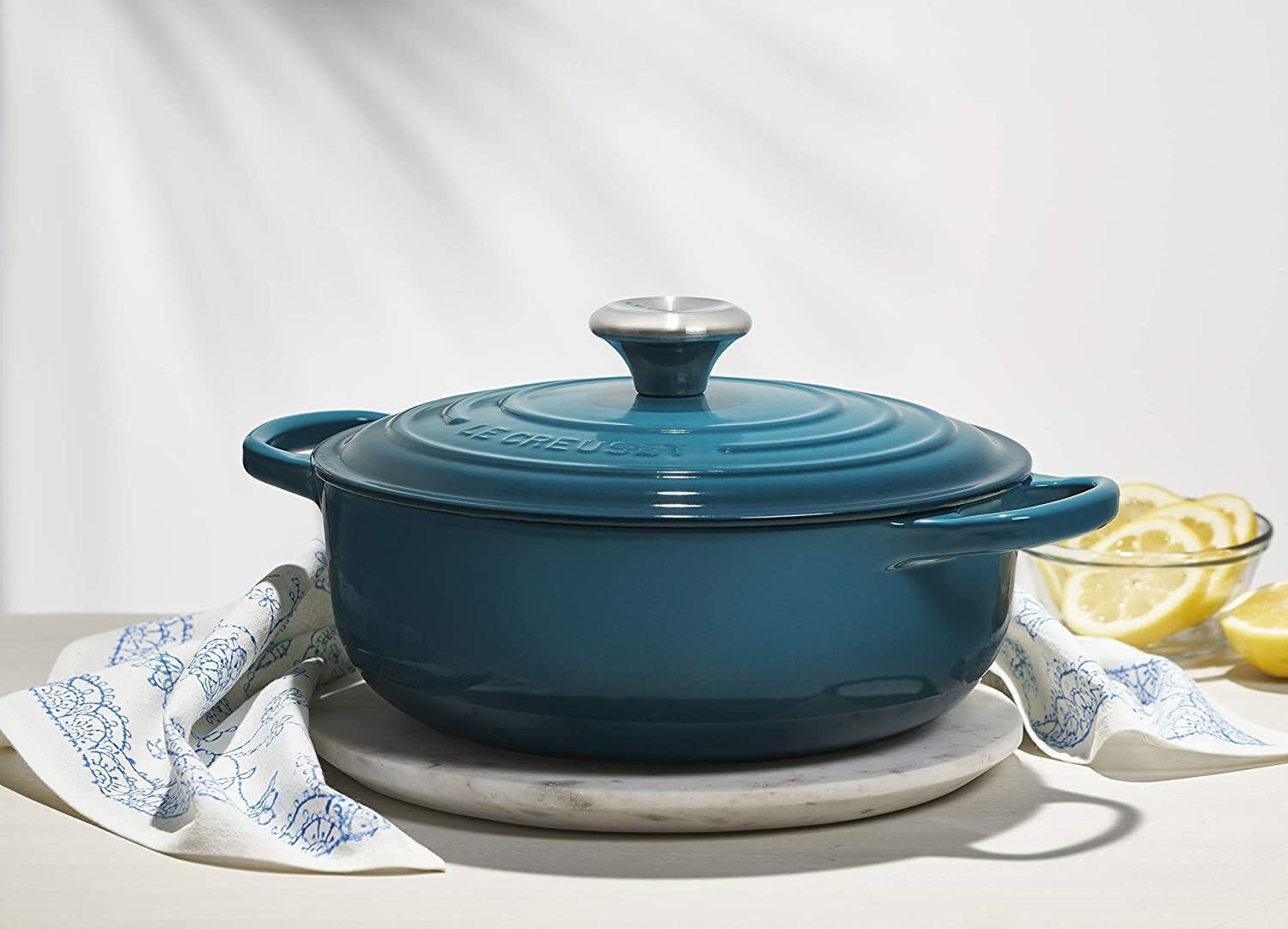 a deep deal le creuset sauteuse wrapped in a dish towel and sitting next to a bowl of sliced lemons
