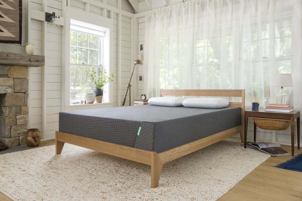 a bare tuft & needle mattress sitting on a wooden bedframe in an airy bedroom