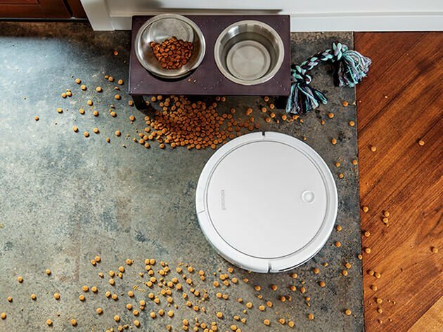 a bissell robot vacuum cleans up a pile of spilled dog food