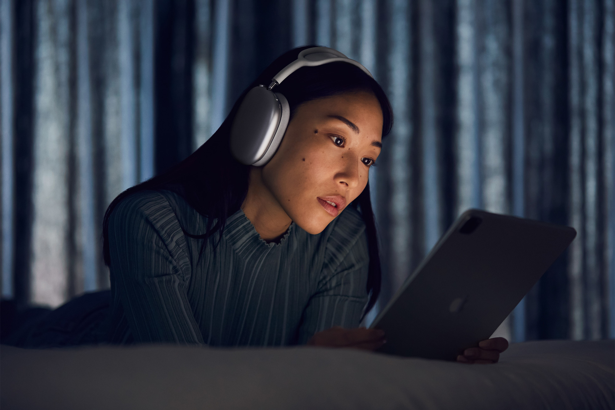 a woman wearing a pair of silver airpods max looks an ipad in a dark room