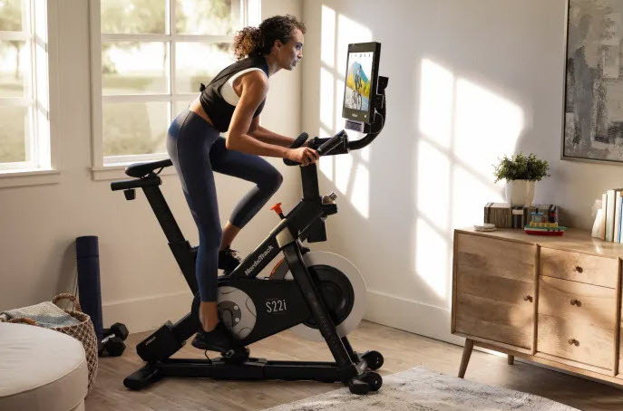 Woman riding on NordicTrack S22i studio cycle in a room. 