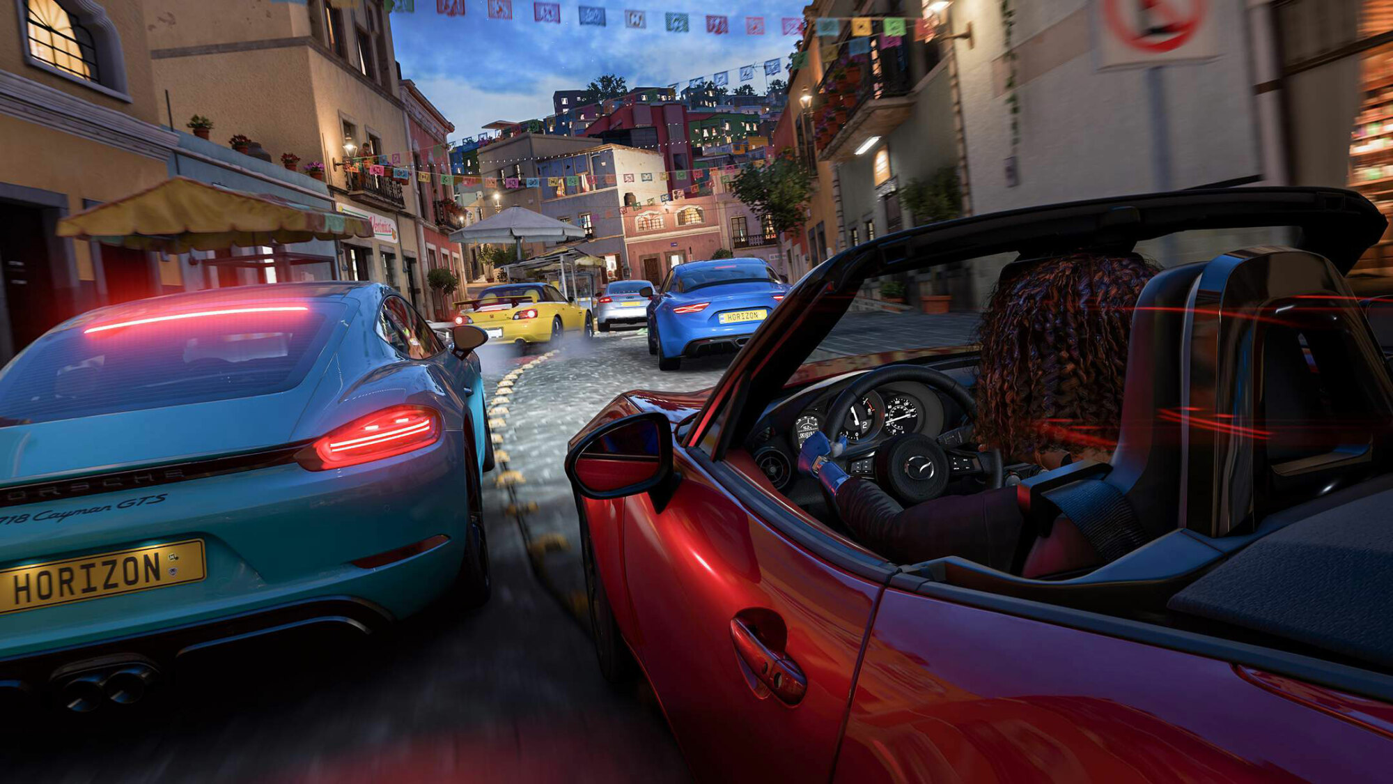 A 'Forza Horizon 5' screenshot with the camera situated just behind a cluster of sports cars as they race through a narrow, cobblestone city street in Mexico.
