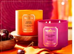 pumpkin spice latte candle and black cherry merlot candle with orange tablecloth and a bowl of cherries