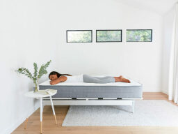 Woman lying on mattress in white room next to houseplant