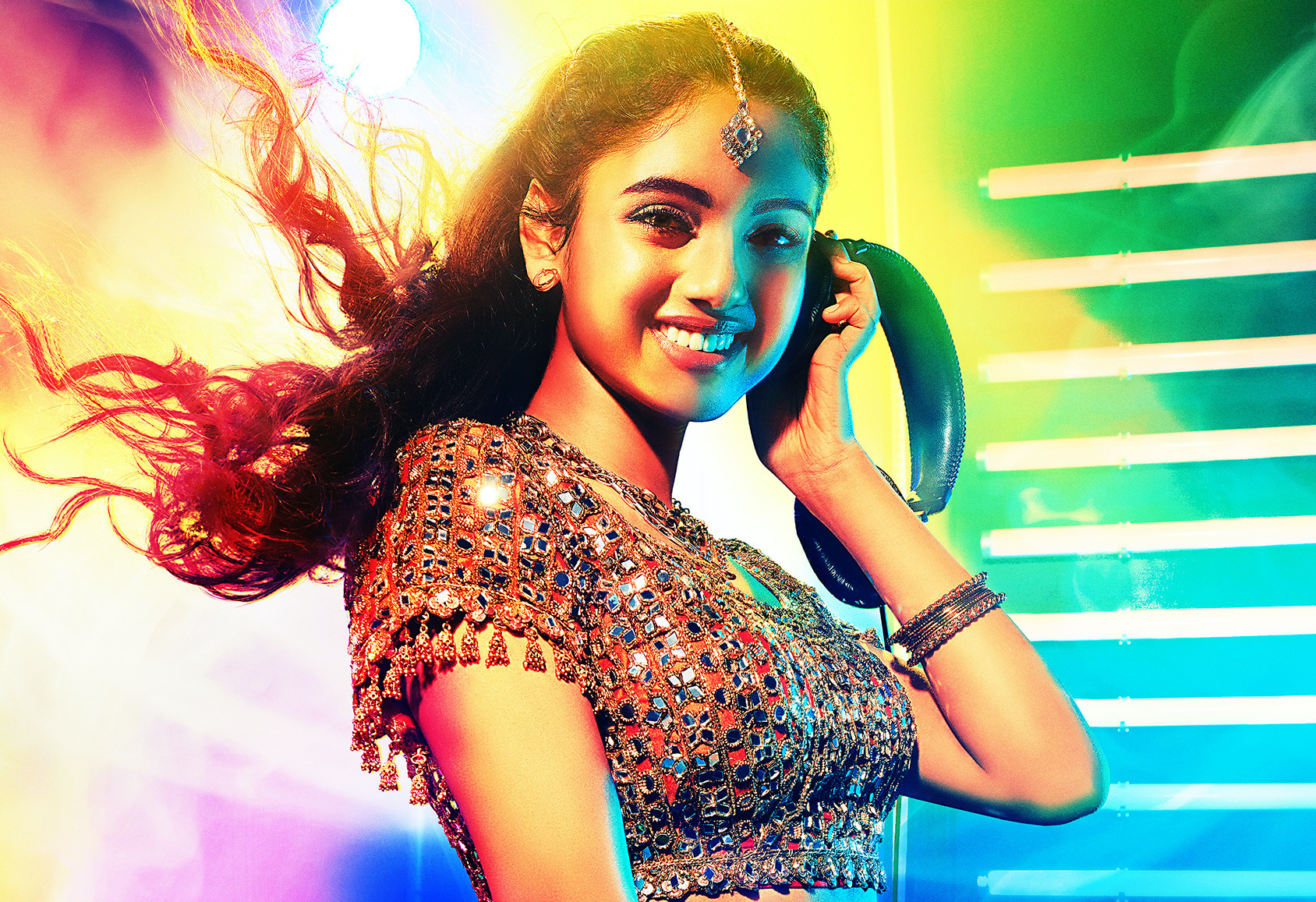 A South Asian teenage girl in an ornate top, spinning as a DJ. Her hair flying in a long ponytail framed against a colorful background for the movie poster.