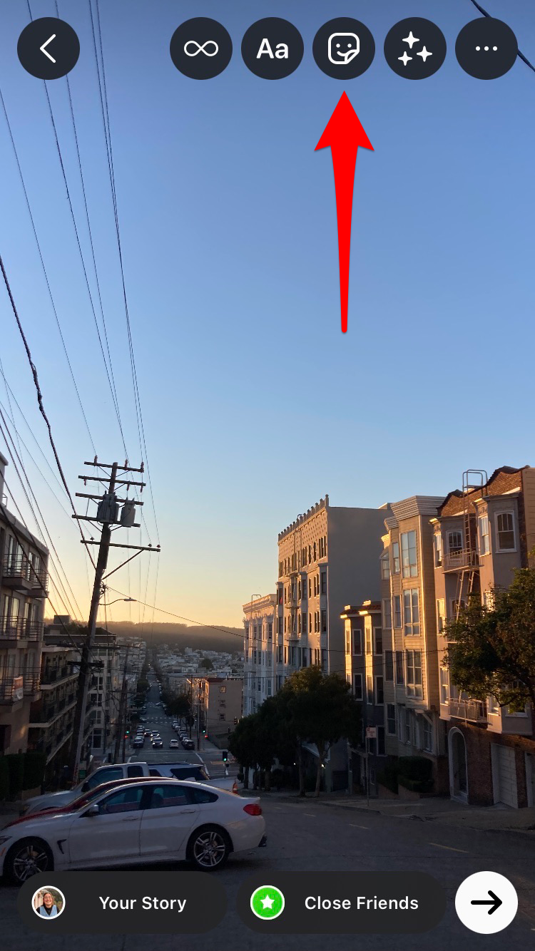 Screenshot of Instagram with an arrow pointing to the square smiley face sticker icon. 