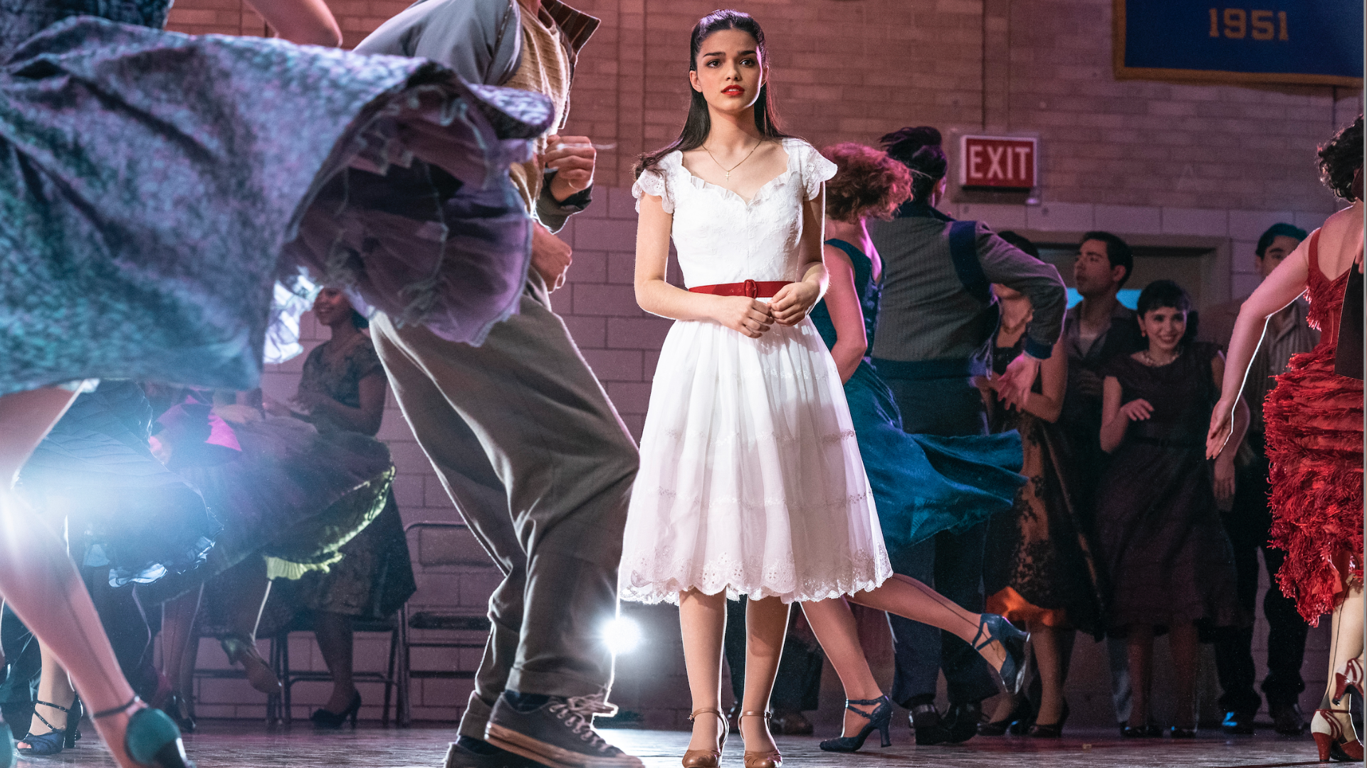 Rachel Zegler as Maria in 'West Side Story' stands in a white dress at a school dance. 