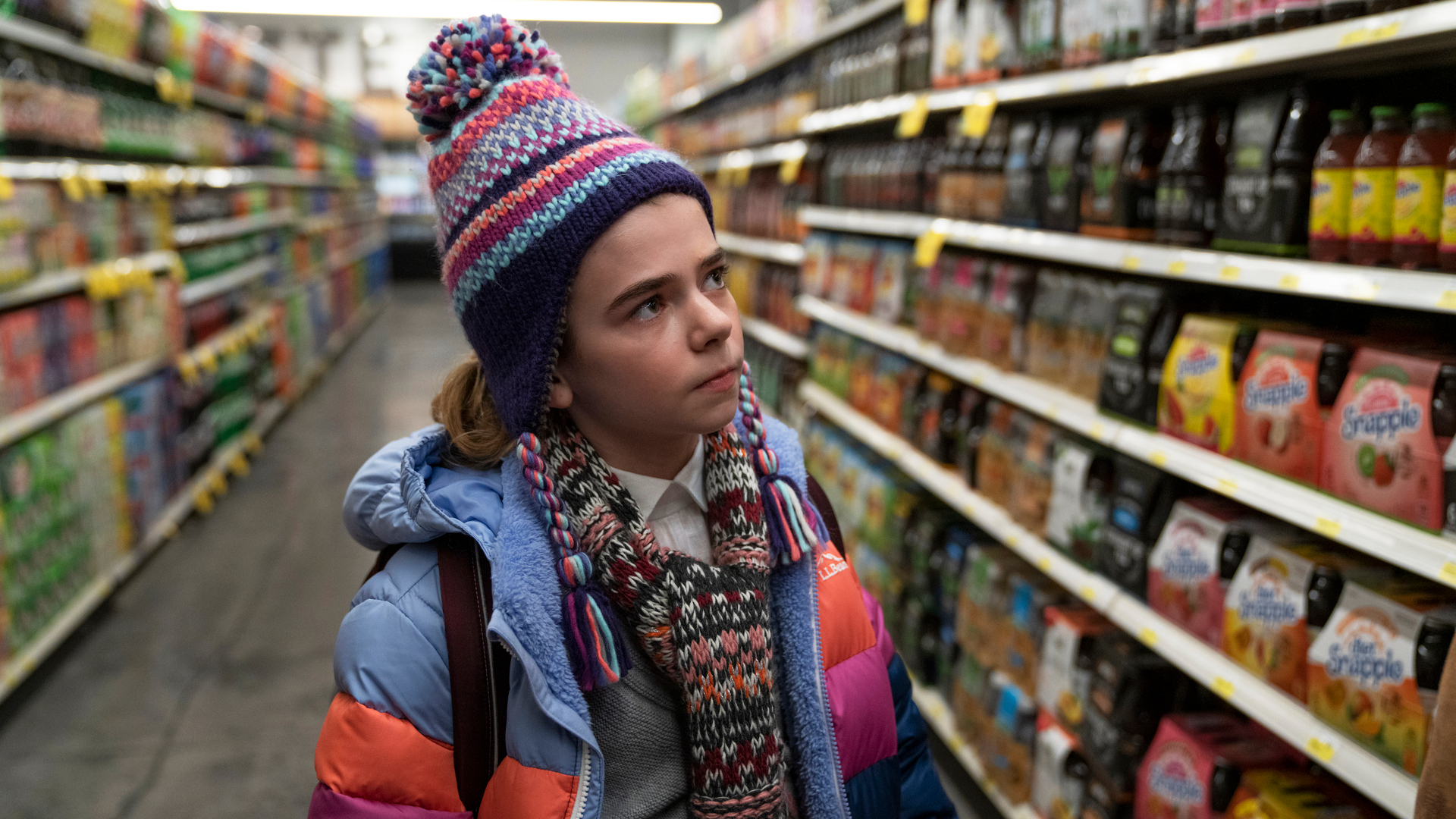 A young girl in winter clothes stands in a grocery store aisle.