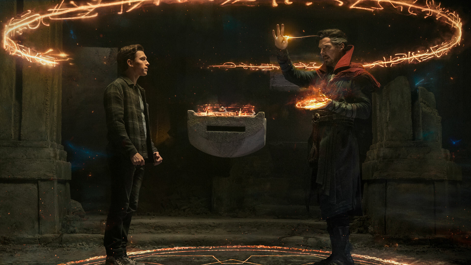 A still from 'Spider-Man: No Way Home' featuring Peter Parker in normal street clothes standing and facing Doctor Strange, who is also standing and facing Parker as he casts a spell. A portal with a glowing fiery orange ring around it hovers above them and a floating stone platform sits between them.