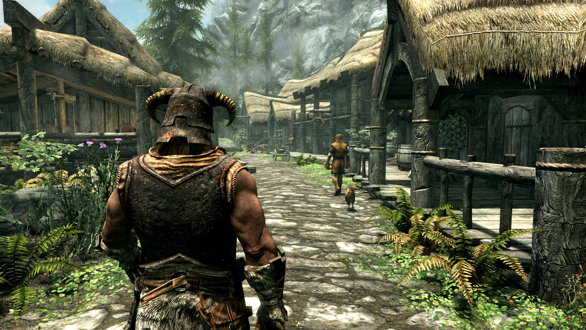 In a screenshot from 'The Elder Scrolls V: Skyrim' a man in a horned helmet, seen from behind, walks through a village of low-lying, thatched roof buildings.