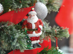 Santa ornament hanging on tree decorated with red ribbon