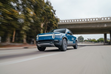 Blue Rivian R1T truck under a freeway crossing.