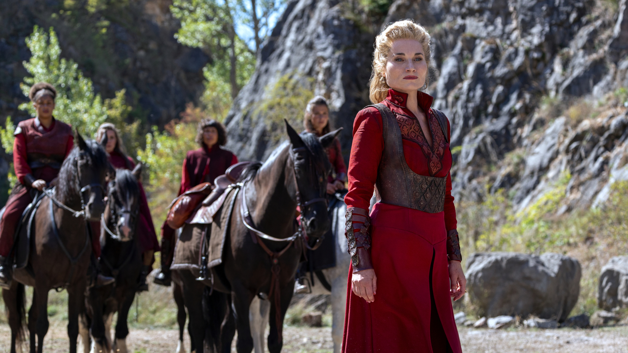 Four omen dressed all in red sit on horses, one woman stands in the foreground.