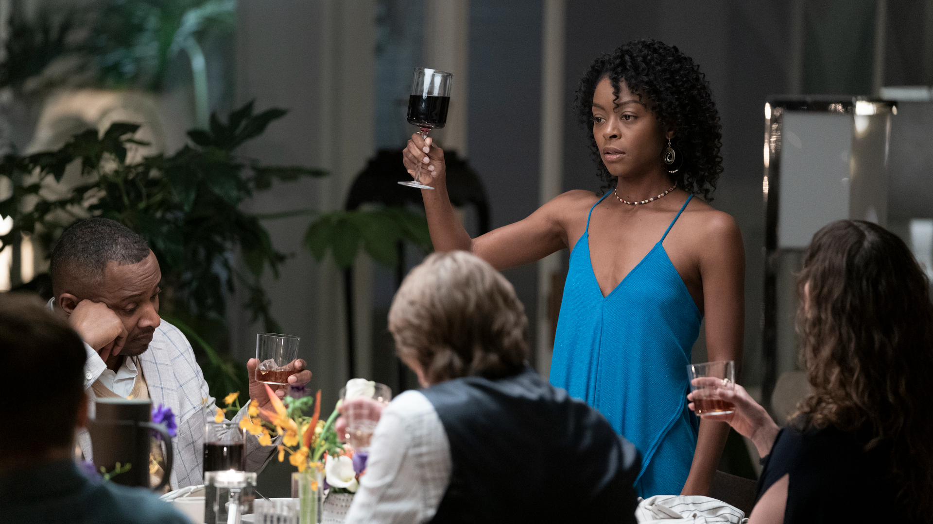 A woman in a blue dress holds up a glass to make a toast.