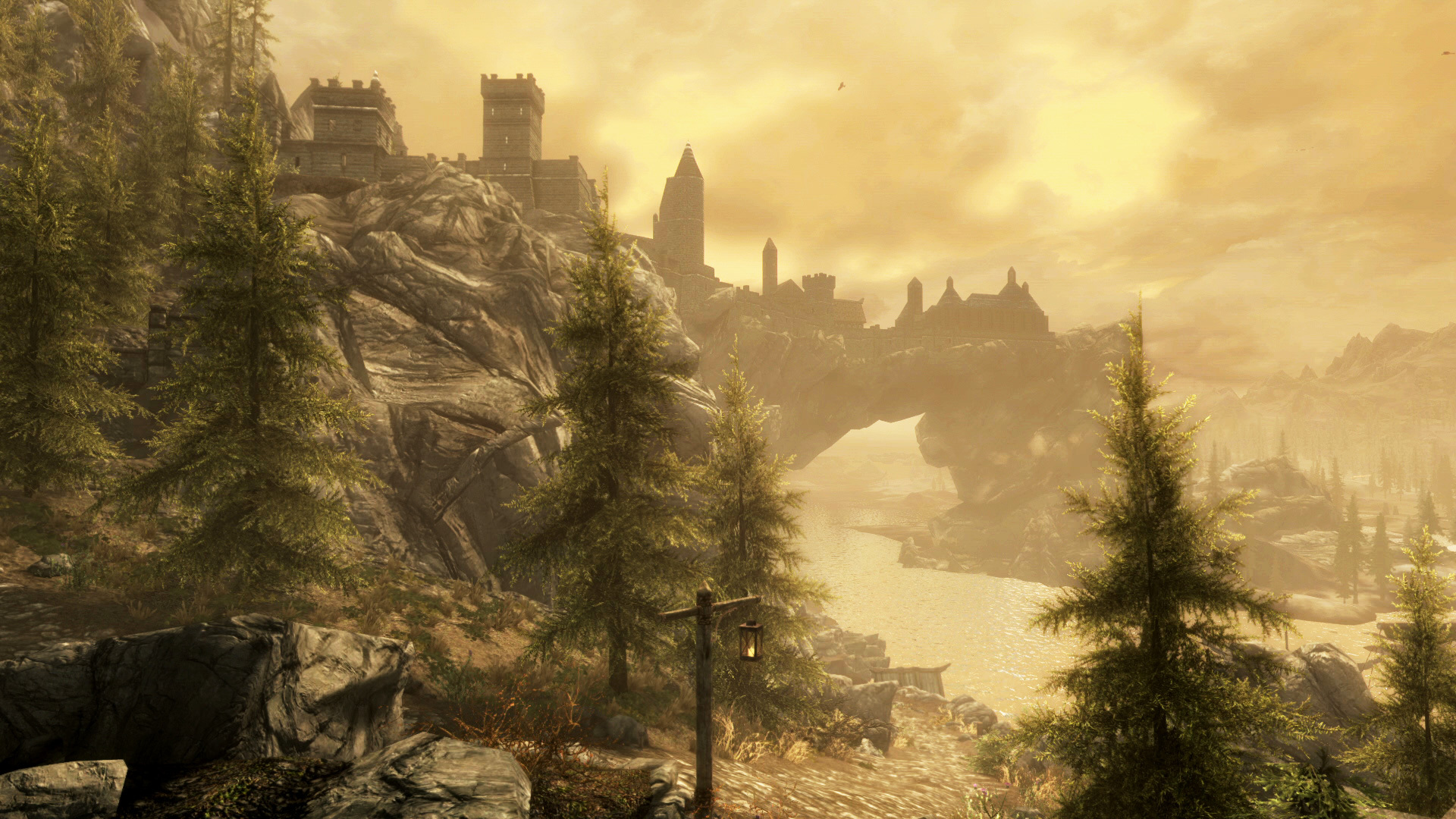 A screenshot from 'The Elder Scrolls V: Skyrim' depicting a landscape scene dominated by tall, green trees in the foreground and, on the horizon, a castle settlement built on top of a mountain that's naturally shaped into an arch above a body of water.