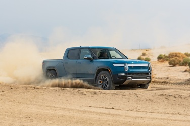 Rivian R1T truck drives through a dusty terrain.