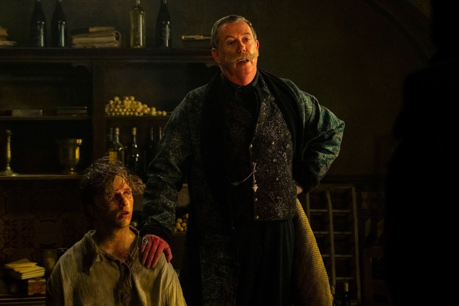 A man rests his hand on another man's shoulders who is on his knees and crying