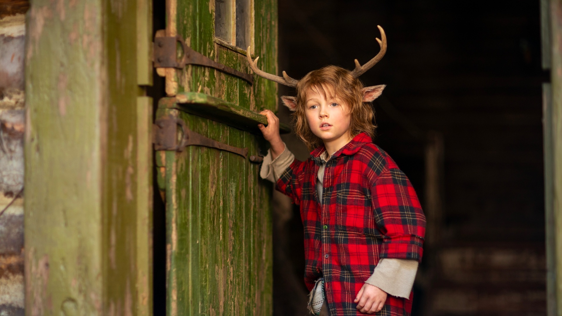 A young boy with antlers stands in a doorway.