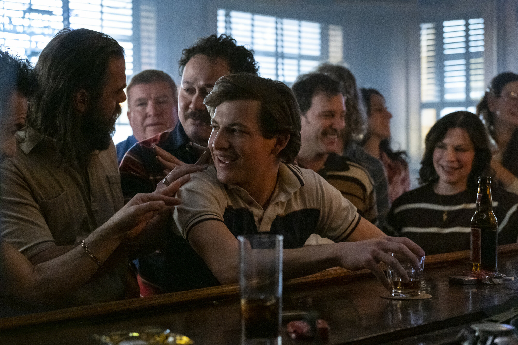 A young man is surrounded by people at a crowded bar in "The Tender Bar." 
