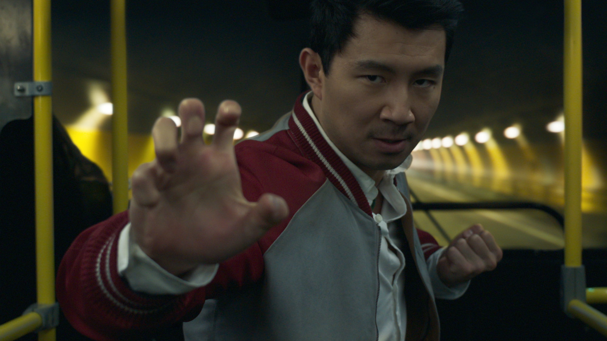 A man in a red jacket takes a fighting stance in the front of a bus