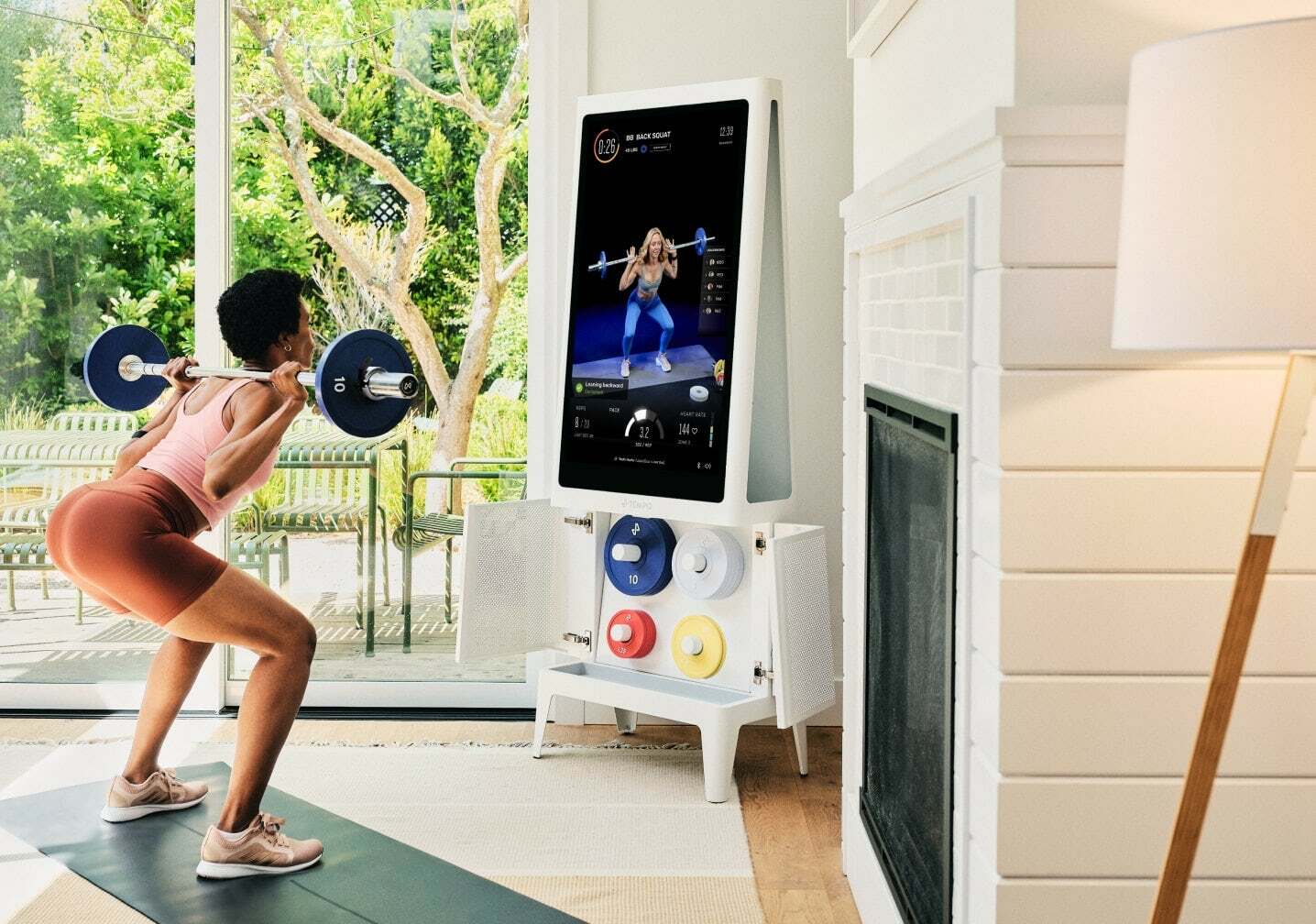 Trainer on a screen that sits atop a cabinet that holds weights and workout equipment.