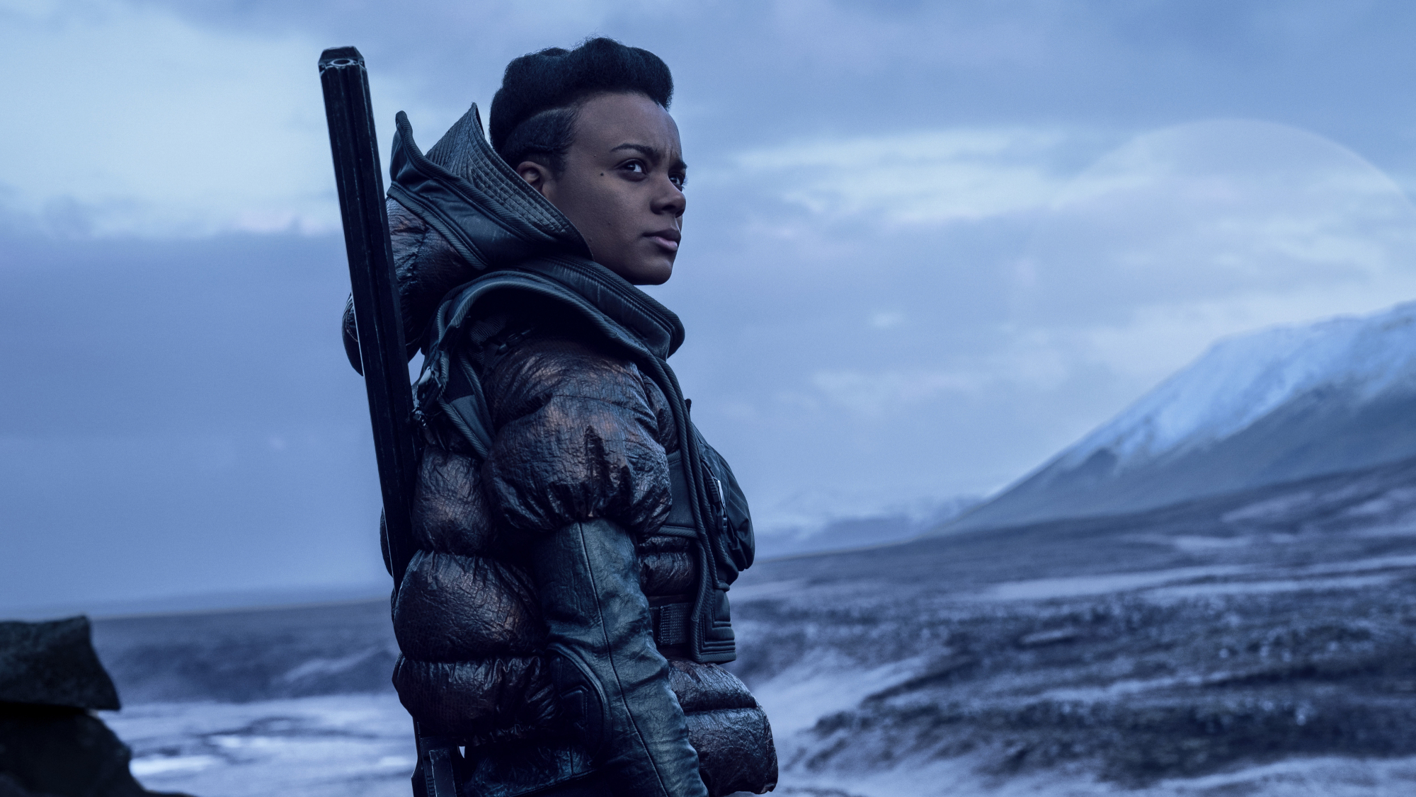 A woman looks out over an icy planet. A moon looms in the background.