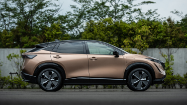 A golden car with trees in the background alongside a white fence.