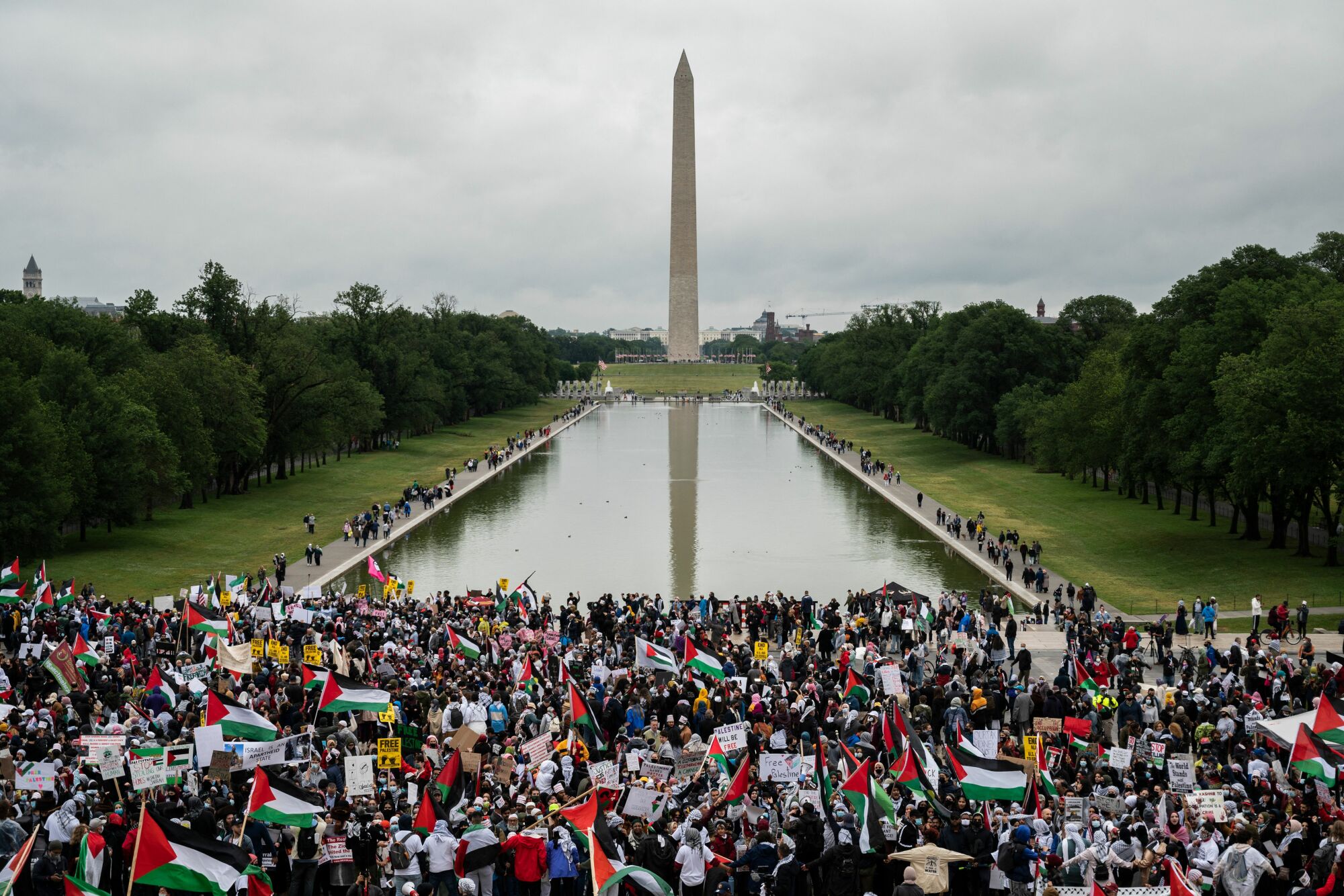 An overhead shot of the Washington memorial, with a large crowd standing in front of the reflection pool.